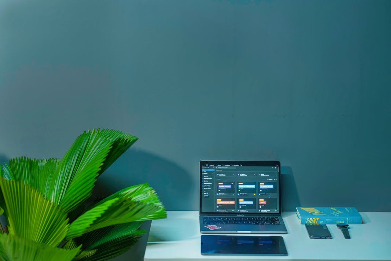 home-hero-1 Sleek office desk setup featuring a laptop, tropical plant, and book in a modern design.