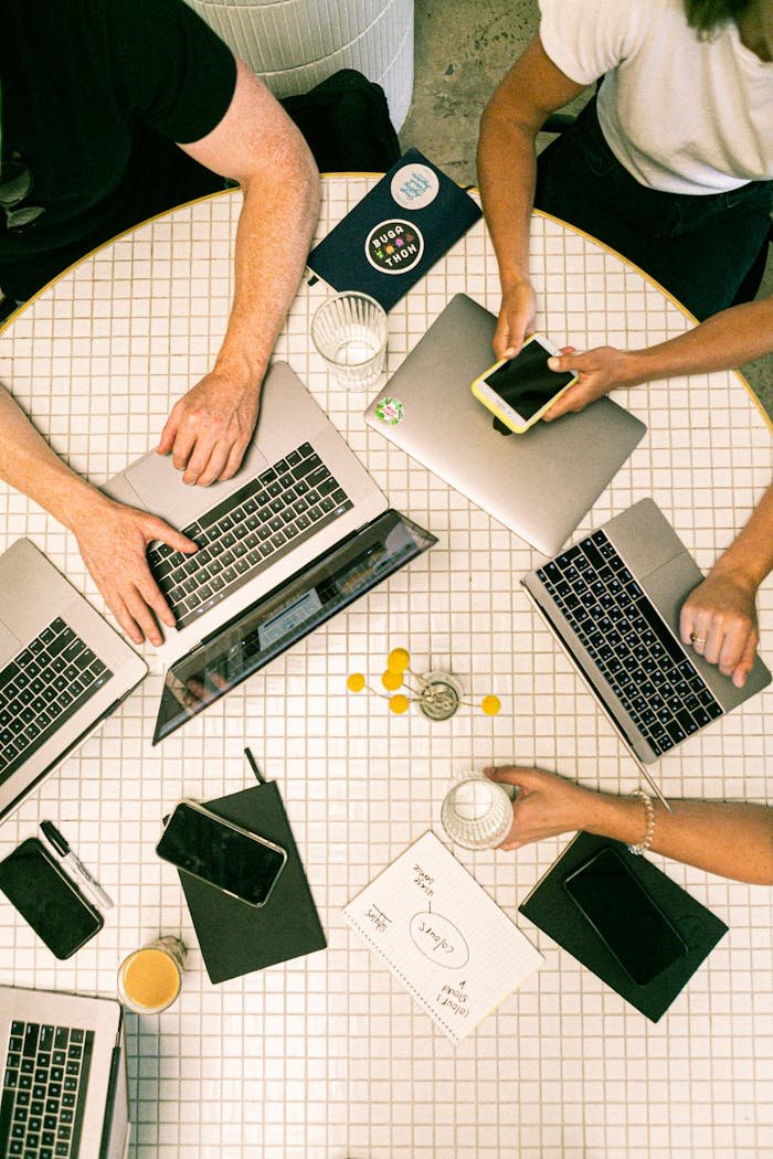 about-us-01 Top view of a team collaborating with laptops, phones, and notes in a modern office.